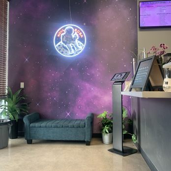 Nova Boba - Nice design layout - Interior of Nova Boba featuring a galaxy-themed wall with a neon astronaut logo, a small teal sofa, and potted plants. - Bubble Tea Near Me - Gilbert, Arizona