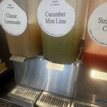 CAVA - Three large beverage dispensers contain Classic Lemonade, Cucumber Mint Lime, and Strawberry Lemonade, with labels indicating flavors and in-house preparation. - Salad Near Me - Jacksonville, Florida