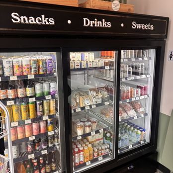 Provisions Thirteen - Cooler - A glass-front refrigerated display case contains drinks, snacks, and desserts, with a sign above indicating sections for snacks, drinks, and sweets. - Bars Near Me - Eugene, Oregon