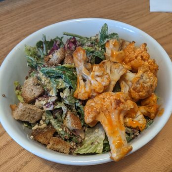Goodbeet - caeser salad with buffalo cauli - next time I will hold the quinoa as I'm just not a quinoa fan, otherwise fantastic - A white bowl filled with a salad featuring roasted cauliflower florets, mixed greens, croutons, and grated cheese, set on a wooden table. The salad includes various leafy greens and crunchy toppings, with the cauliflower having an orange-colored sauce or seasoning. - Vegan Near Me - Haddon Township, New Jersey
