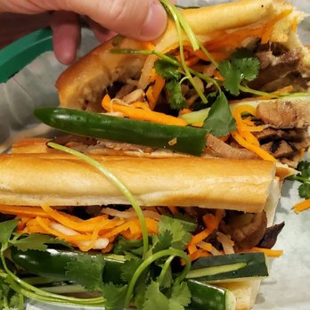 Pho Bar - Pork banh mi - Two banh mi sandwiches filled with meat, vegetables, and herbs are placed on a green tray lined with white paper. - Vietnamese Near Me - Rio Rancho, New Mexico