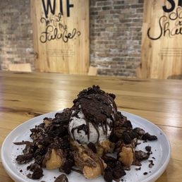 Churros - A dessert featuring a scoop of ice cream topped with chocolate drizzle, surrounded by cookie crumbles and chocolate pieces, served on a white plate.