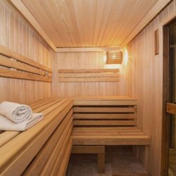 A spacious cedar-lined dry sauna features tiered wooden benches, soft lighting, and neatly folded towels...