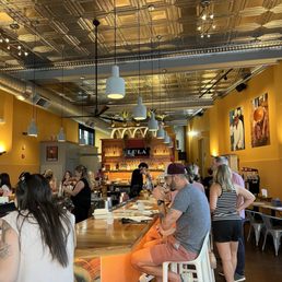 Inside Lula, a Mexican eatery, customers are seated at a bar with a golden ceiling and yellow walls, enjoying drinks and conversation.