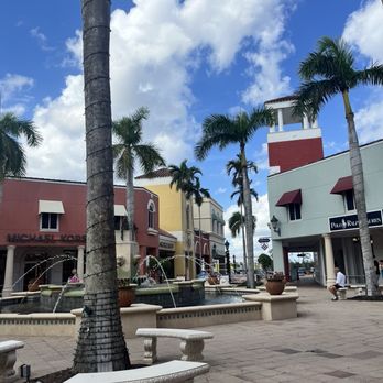 Miromar Outlets - A shopping plaza with palm trees, water fountains, and storefronts including Michael Kors and Polo Ralph Lauren, under a partly cloudy sky. - Shopping Centers Near Me - Estero, Florida