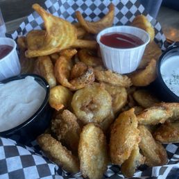 Fried Pickles & Spudnik Basket - A basket of fried pickles, onion rings, and chicken tenders served with various dipping sauces, on checkered paper at a restaurant.