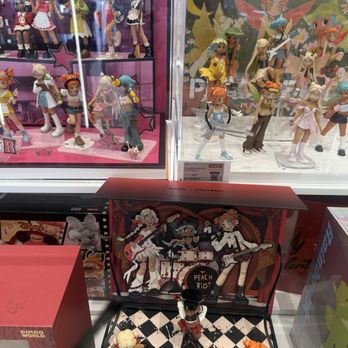 Pop Mart - The image shows multiple display cases with collectible figurines from popular animated series, including characters from 'Poppy,' 'Peach Riot,' Disney, and other franchises. The figurines are arranged on shelves and platforms, with some in dynamic poses. There are also boxed collectibles and a decorative backdrop featuring animated characters. The display appears to be in a retail store specializing in pop culture merchandise. - Toy Stores Near Me - Oak Brook, Illinois