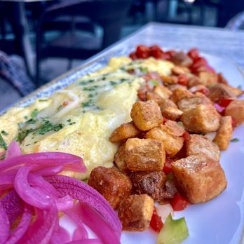 Herbie's Restaurant - A close-up of a plate with fried tofu cubes, scrambled eggs with herbs, pickled red onions, and chopped vegetables, served outdoors. - New American Near Me - Clayton, Missouri