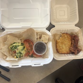 Byte & Coffee - On the left is the egg white cup & the hash brown & bacon are on the right. - The image shows two foam takeout containers on a table. The left container holds scrambled eggs topped with green herbs, sliced tomatoes, and a small cup of syrup. The right container contains a hash brown and several strips of bacon. The containers are open, revealing the food inside, and the setting appears to be a casual dining or takeout environment. - Coffee & Tea Near Me - Pompano Beach, Florida