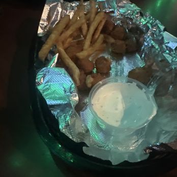 Patsy’s Pub - A tray with fried food, French fries, and a cup of dipping sauce on a dark table, likely at a sports bar or pub. - Salad Near Me - Westfield, Indiana