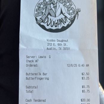 Voodoo Doughnut - Receipt for purchase. - A printed receipt from Voodoo Doughnut located at 212 E. 6th St., Austin, TX, features the business logo at the top, depicting a skeleton in a hat with doughnuts in the background. The receipt lists the server's name, check number, order date and time, items purchased (Buttermilk Bar and Butterfingering), their prices, subtotal, total, and payment amount tendered with change. The receipt includes a note about ordering via the business website for pickup or carside service. - Donuts Near Me - Austin, Texas