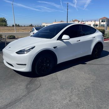 Midnight Window Tint - 20% Front windows and windshield 35% - A white Tesla Model Y with tinted windows is parked on a paved lot under a clear blue sky with visible contrails. - Car Stereo Installation Near Me - Banning, California