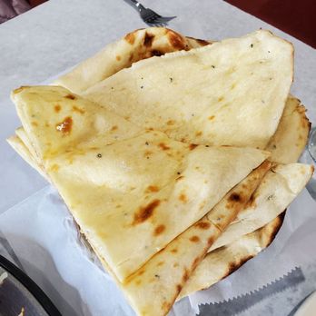 Saffron Restaurant - Several pieces of naan bread are stacked on a tray lined with white paper, with a fork and a tablecloth visible in the background. - Indian Near Me - Bloomingdale, Illinois