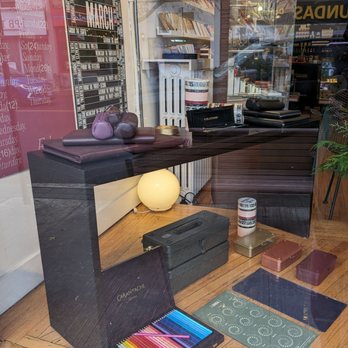 Take Note - This store sells Blackwing pencils. - The display showcases colored pencils, notebooks, and desk accessories arranged on a wooden surface, with books and a lamp visible inside the store. - Cards & Stationery Near Me - Toronto, Ontario