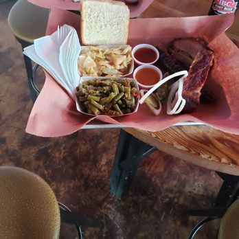 Brown's Bar-B-Que - A tray of barbecue food includes sliced meats, bread, pickles, green beans, and sauces, served on a pink paper liner on a wooden table. - Barbeque Near Me - Austin, Texas