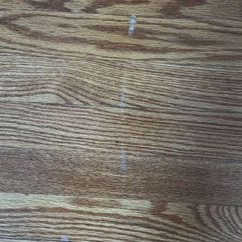 Arch Moving - Scratch in hardwood - A close-up image of a wooden surface, likely a table or floor, showing a visible scratch running vertically through the wood grain. The surface has a natural wood finish with distinct grain patterns and some minor damage or scuff marks near the bottom left corner. - Movers Near Me - Saint Ann, Missouri