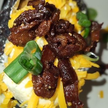 Pappadeaux Seafood Kitchen - A baked potato is topped with crispy bacon, shredded cheddar cheese, chopped green onions, and sour cream, served in foil. - Seafood Near Me - Albuquerque, New Mexico