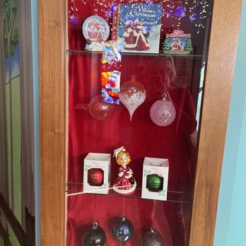 Behringer-Crawford Museum - A glass display case contains Christmas ornaments, decorations, and holiday-themed items, set against a red background with string lights and festive packaging. - Museums Near Me - Covington, Kentucky