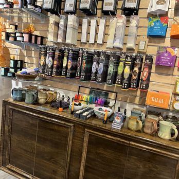 Becca Rose - Herbal teas, candles, and ceramic mugs are arranged on a wooden counter in a metaphysical shop, with various packaged products and colorful pens. - Women's Clothing Near Me - Mystic, Connecticut