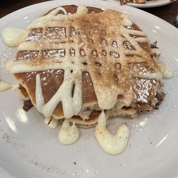 Pomegranate Restaurant - Cinnamon Roll Pancakes - Stacked pancakes with white chocolate drizzle, powdered sugar, and dollops of cream on a white plate, served at a family-friendly restaurant. - American Near Me - Aurora, Illinois