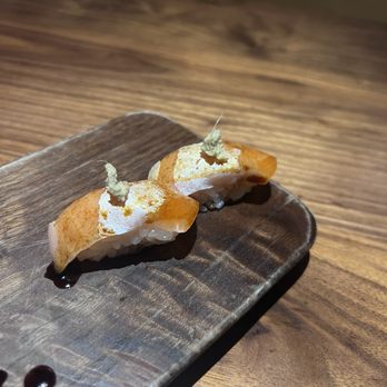 Uchi Miami - Salmon belly - Two sushi pieces with salmon topping and wasabi garnish are placed on a wooden serving plate, with soy sauce drops nearby. - Japanese Near Me - Miami, Florida