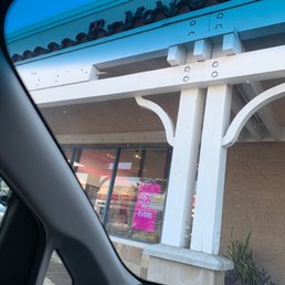 The image shows a storefront with large glass windows displaying a pink promotional sign, taken from inside a vehicle.