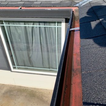 Merced Window Cleaning - After - The image shows a rooftop window with a metal railing, surrounded by asphalt shingles and roofing materials, with shadows cast on the roof. - Window Washing Near Me