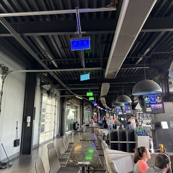 Topgolf - A modern indoor bar or lounge with seating, digital signs hanging from the ceiling, and multiple screens displaying content. - New American Near Me - Albuquerque, New Mexico