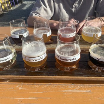 Funkwerks - Flight in front row is Boutique Flight, back row Sour Snack Pack Flight. - Two wooden paddles hold eight beer flights with different beers, each labeled with 'funkwerks,' on a wooden table outdoors. - Breweries Near Me - Fort Collins, Colorado