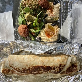 Jerusalem Organic Kitchen - A takeout Middle Eastern meal includes a large wrap on foil and a plastic container with falafel, hummus, and salad, accompanied by small containers of sauces. - Middle Eastern Near Me - Berkeley, California