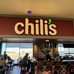 Entrance - Interior of Chili's restaurant with seating, a bar, and a view of the airport runway through large windows.