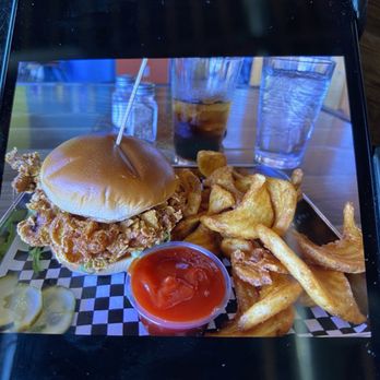 The Kosmos - Fried Chicken Sandwich & Cool looking Fries! - A fried chicken sandwich with a bun, fried chicken, and lettuce is served with a side of fries, ketchup, and drinks on a tray at a restaurant. - Bars Near Me - Albuquerque, New Mexico