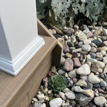 Elite Exteriors - This side is much longer than the other. - A succulent plant is growing in a rocky garden bed next to a wooden structure with a white base. - Roofing Near Me - New Berlin, Wisconsin