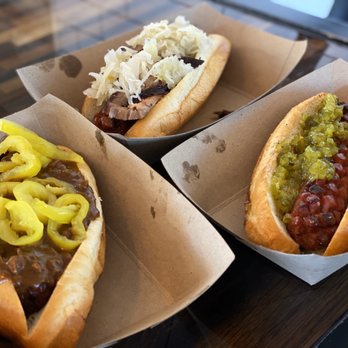 Caldwell County Mexi-Q - Clockwise from bottom left: Chili Dawg with banana pepper, Brosket Dawg with sauerkraut, regular dawg with relish. - Barbeque Near Me - Gilbert, Arizona Caldwell County Mexi-Q - Clockwise from bottom left: Chili Dawg with banana pepper, Brosket Dawg with sauerkraut, regular dawg with relish. - Barbeque Near Me - Gilbert, Arizona