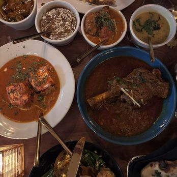 Bricklane Curry House, Upper Montclair, NJ - Assorted Indian dishes including curries, rice, and appetizers are displayed on a wooden table, with utensils and a glass of wine. - Indian Near Me - Montclair, New Jersey
