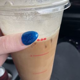 What I received. Only took one sip. - A person holds a large iced coffee in a clear plastic cup with a lid, showing a light brown beverage with ice, against a dark background.