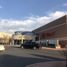 Outside - The image depicts the exterior of a Target retail store in El Paso, TX, with a parking lot in the foreground. Several cars are parked, including a black pickup truck and a white sedan. A few shoppers are seen walking near the entrance, which is decorated with holiday garlands. The building features the Target logo and signage, with a clear blue sky and some clouds overhead. The scene suggests a typical shopping day outside the retail store.