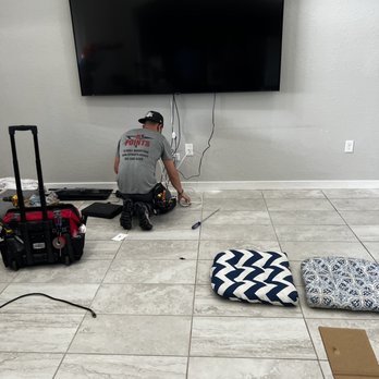 5 Points TV Installations - A technician is working on a wall-mounted flat-screen TV in a room with tiled flooring, tools, and cushions on the floor. - TV Mounting Near Me