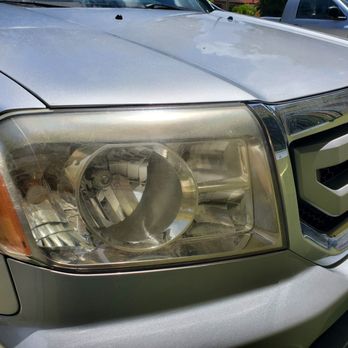 Fixbodycar - A vehicle's front end, including the headlight and grille, is shown with visible dirt and some wear, parked outdoors. - Body Shops Near Me
