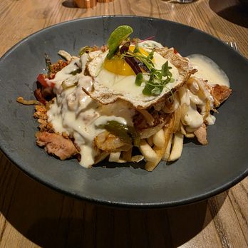Corinne - Philly Chicken Bowl - A plated dish featuring fries, grilled meat, creamy sauce, and a fried egg garnished with microgreens, served in a restaurant setting. - Breakfast & Brunch Near Me - Denver, Colorado
