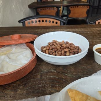 El Arroyo - Delicious whole beans and homemade flour tortillas and salsa. - A wooden table holds a white bowl of beans, a small cup of salsa, and a basket with a tortilla inside, in a restaurant setting. - Mexican Near Me - Murphys, California