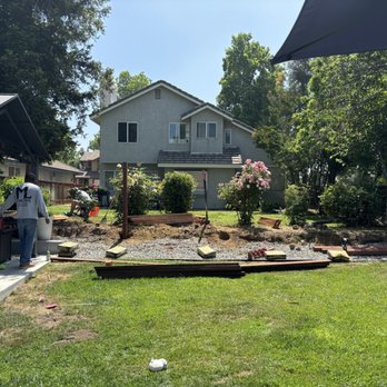 Ergeon - During - Construction workers are building a pathway or patio in a backyard, with tools and materials visible, in front of a house with a garden. - Fences & Gates Near Me - Riverside, California