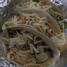 three tacos in foil with cheese and lettuce
