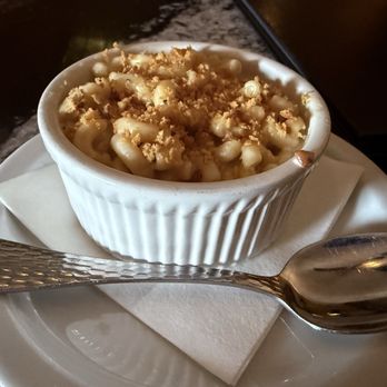 ALC Steaks - A small white ramekin filled with macaroni and cheese topped with breadcrumbs, placed on a white plate with a napkin and a spoon. - Steakhouses Near Me - Austin, Texas