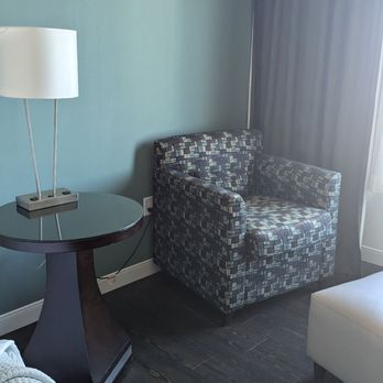Hotel Indigo Waco - Baylor - A chair, and ottoman with a table and lamp with many plugs - Hotels Near Me - Waco, Texas