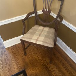 Before - A wooden chair with a decorative backrest and plaid fabric seat is positioned in a corner near a wall with white trim and hardwood flooring.