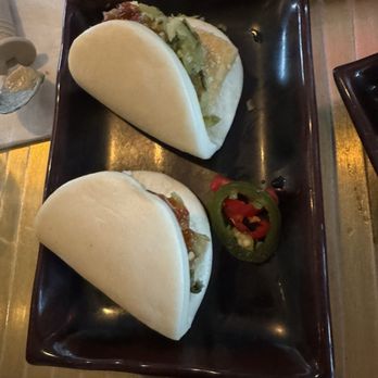 Myers & Chang - Bao - Two steamed bao buns filled with ingredients are placed on a black rectangular plate, accompanied by sliced jalapeño peppers. - Asian Fusion Near Me - Boston, Massachusetts