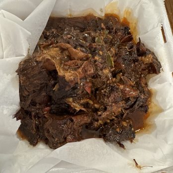 Jerky Jerk - Ox tail - Ox tail served in a foam takeout container with parchment paper lining, featuring dark, braised meat with sauce. - Caribbean Near Me - Rolling Meadows, Illinois