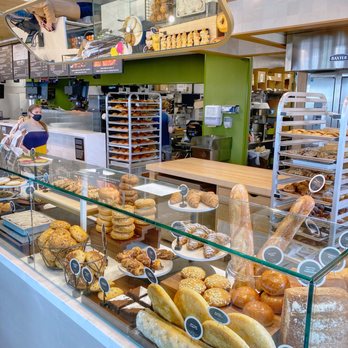 Panera Bread - Bakery or cafe display case showcasing an assortment of bread, pastries, and baked treats with a busy kitchen in the background. - Sandwiches Near Me - Wheaton, Illinois