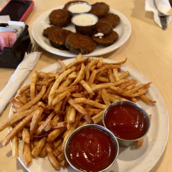 Holy Burgers - Appetizers, fried zucchini and fries - A plate of French fries with two cups of ketchup and a plate of fried zucchini with dipping sauces on a table at a casual dining restaurant. - Burgers Near Me - Albuquerque, New Mexico